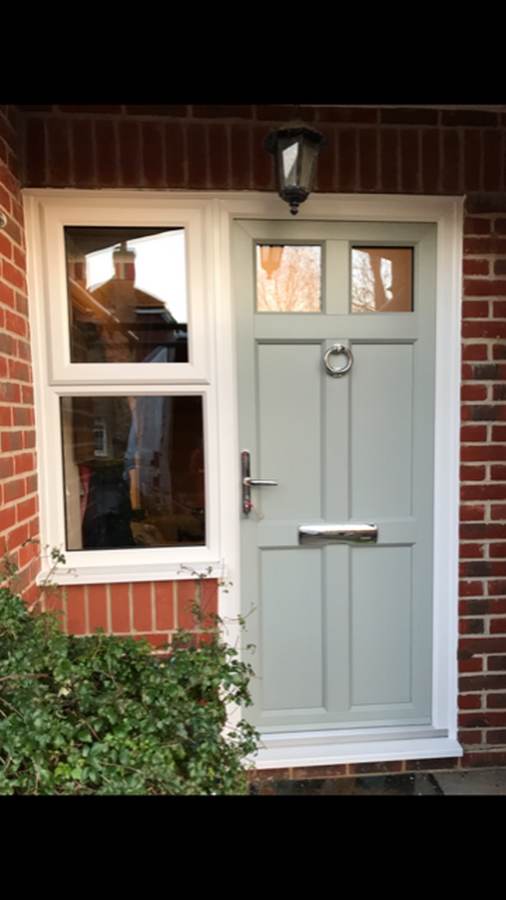 Light grey composite front door with glazed top panels installed beside a white framed window in a brick property entrance.