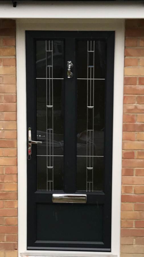 Black composite front door with decorative glazed panels and chrome letterbox fitted to a brick property entrance.