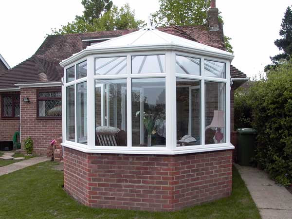 White framed conservatory with large double glazed windows and brick base installed on a detached property.