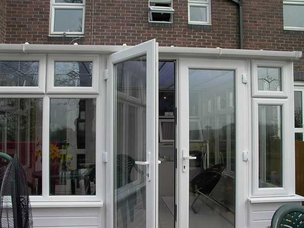White UPVC conservatory with double glazed doors and side windows installed at the rear of a brick home.